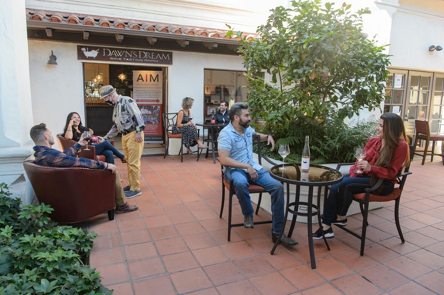 People sitting at tables on a brick patio in front of a white building